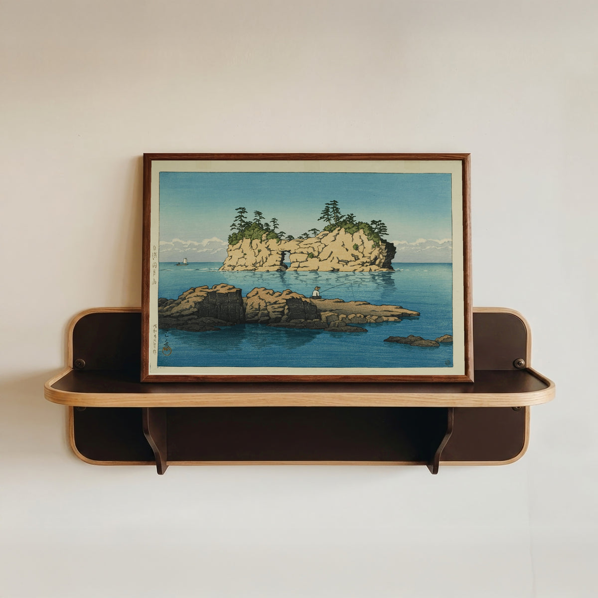 Framed art print of Engetsu Island, Shirahama by Kawase Hasui, in a dark wood frame resting on a wall shelf