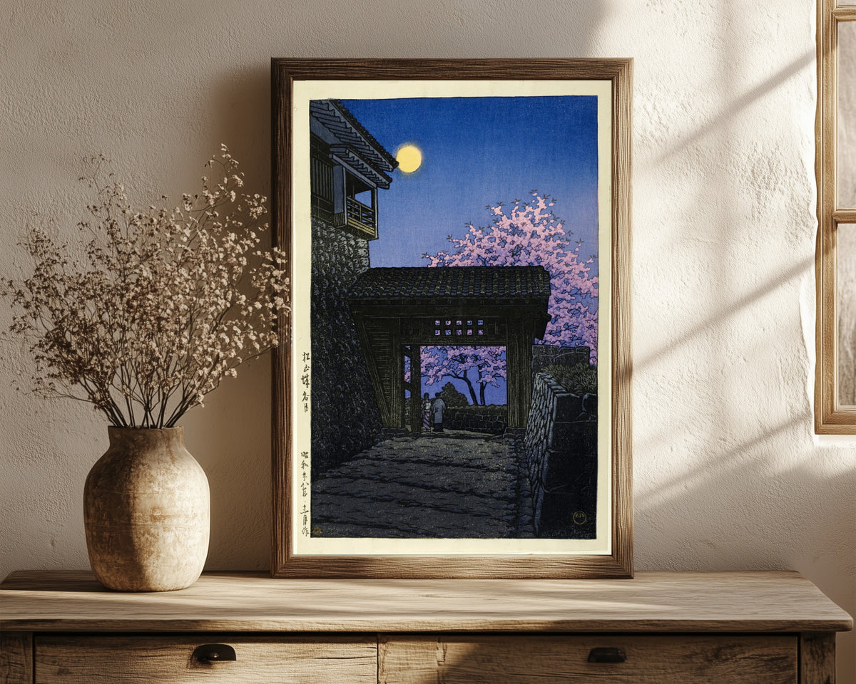 Framed art print of Evening at Matsuyama Castle by Kawase Hasui, in a dark wood frame leaning on a rustic console beside dried flowers