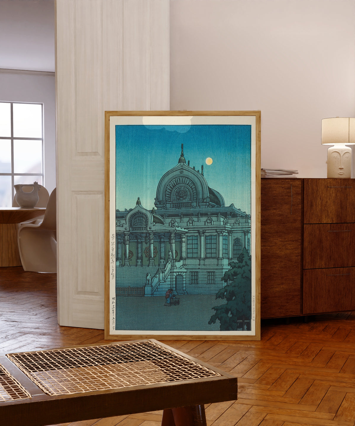 Framed art print of Evening Moon at Honganji Temple, Tsukiji by Kawase Hasui, in a light wood frame leaning in a warm room with a parquet floor