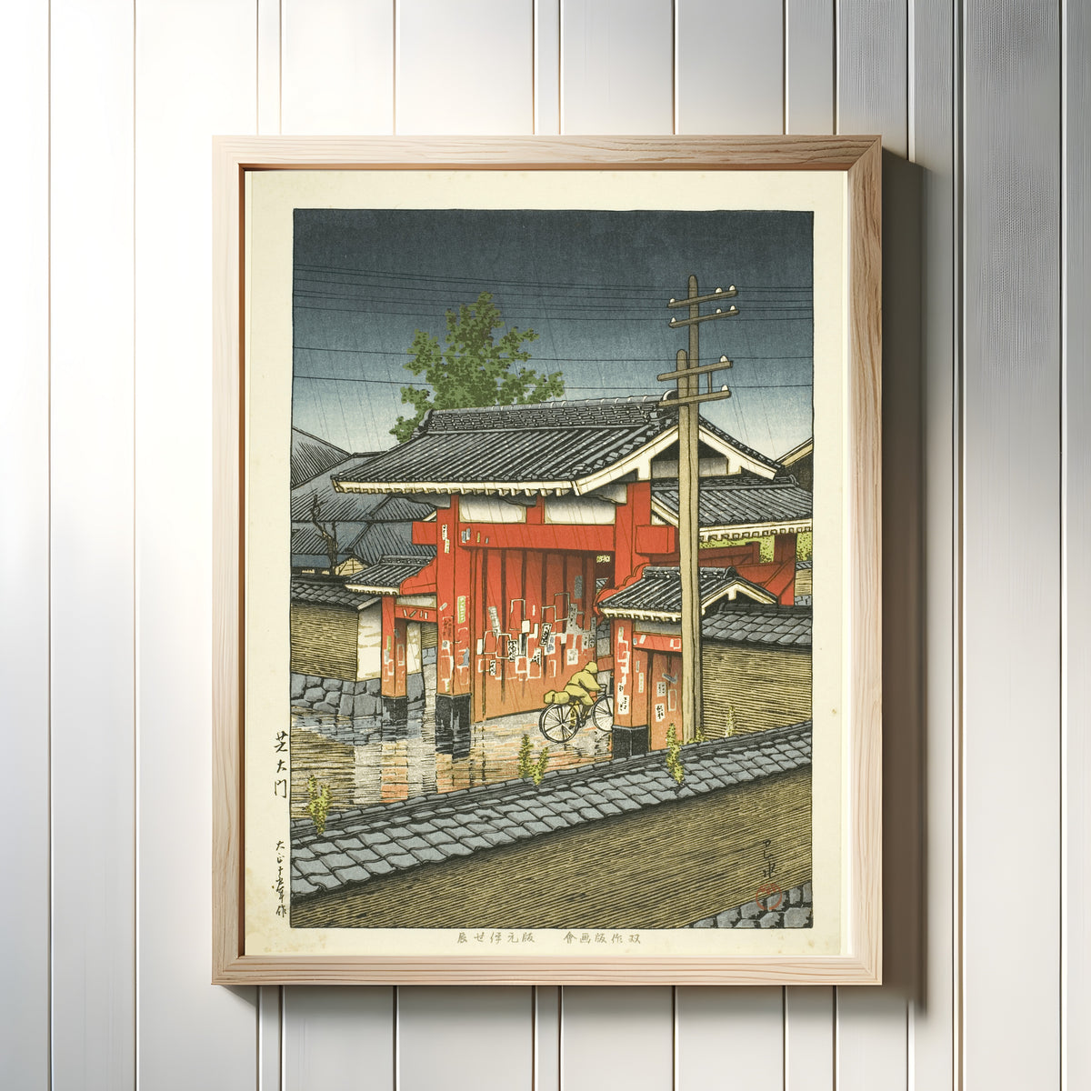 Framed art print of Great Gate at Shiba by Kawase Hasui, in a light wood frame on a white panelled wall