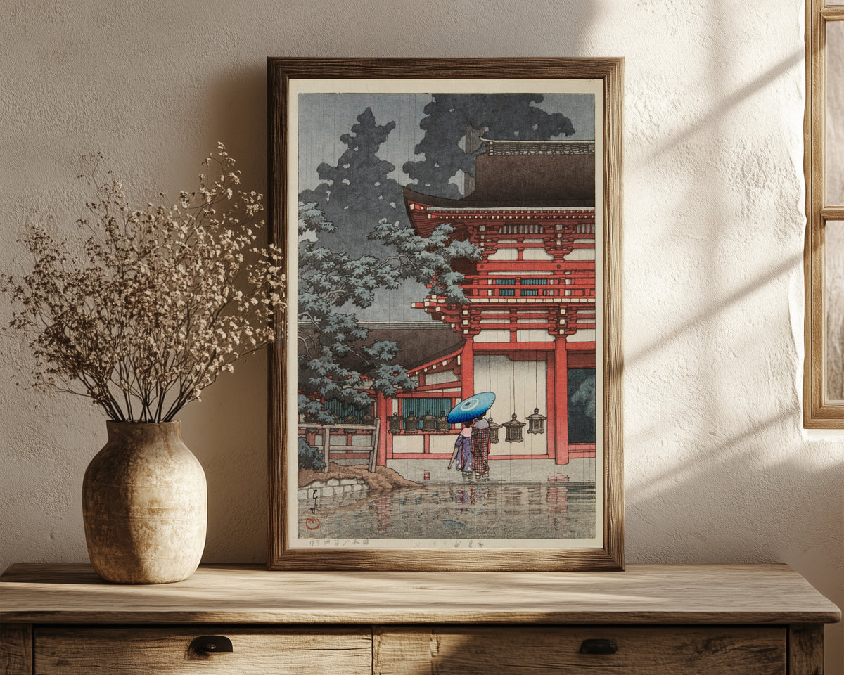 Framed art print of Kasuga Shrine, Nara by Kawase Hasui, in a dark wood frame leaning on a rustic console beside dried flowers
