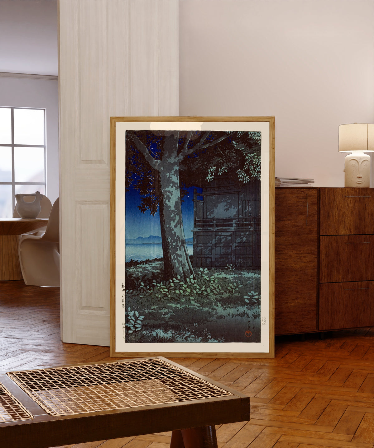 Framed art print of Lake Hachirogata at Night by Kawase Hasui, in a light wood frame leaning in a warm room with a parquet floor