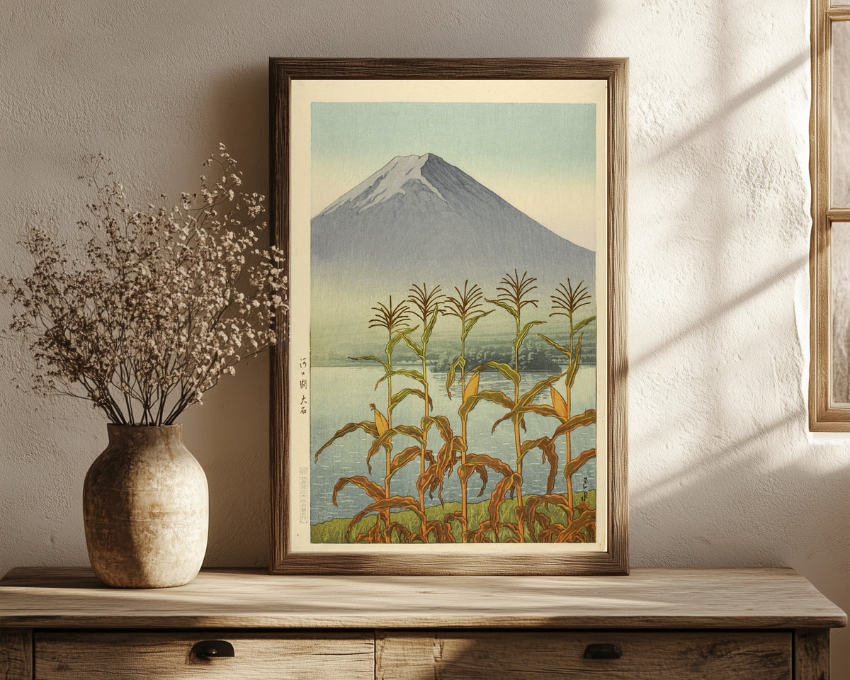 Framed art print of Lake Kawaguchi, Oishi by Kawase Hasui, in a dark wood frame leaning on a rustic console beside dried flowers