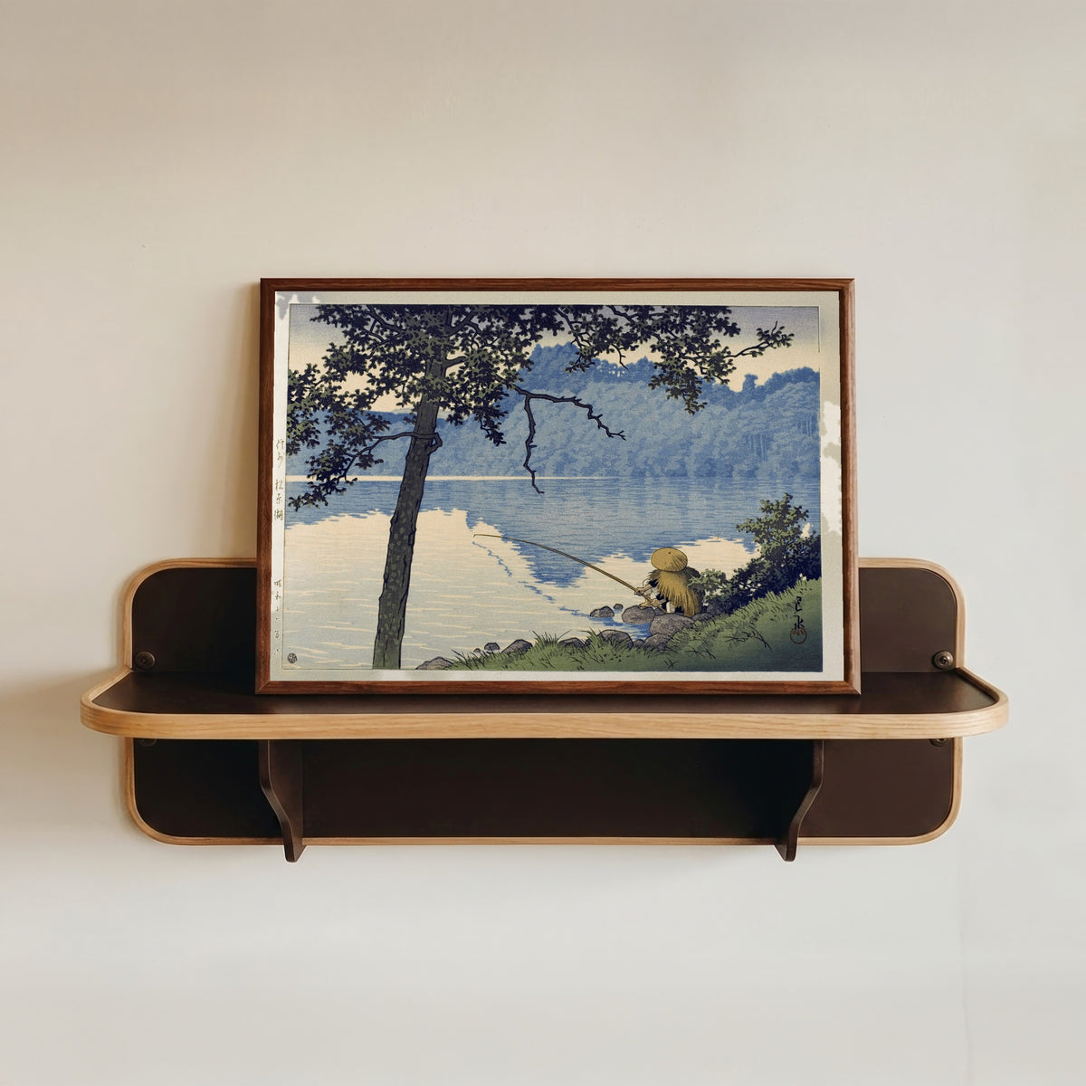 Framed art print of Lake Matsubara by Kawase Hasui, in a dark wood frame resting on a wall shelf