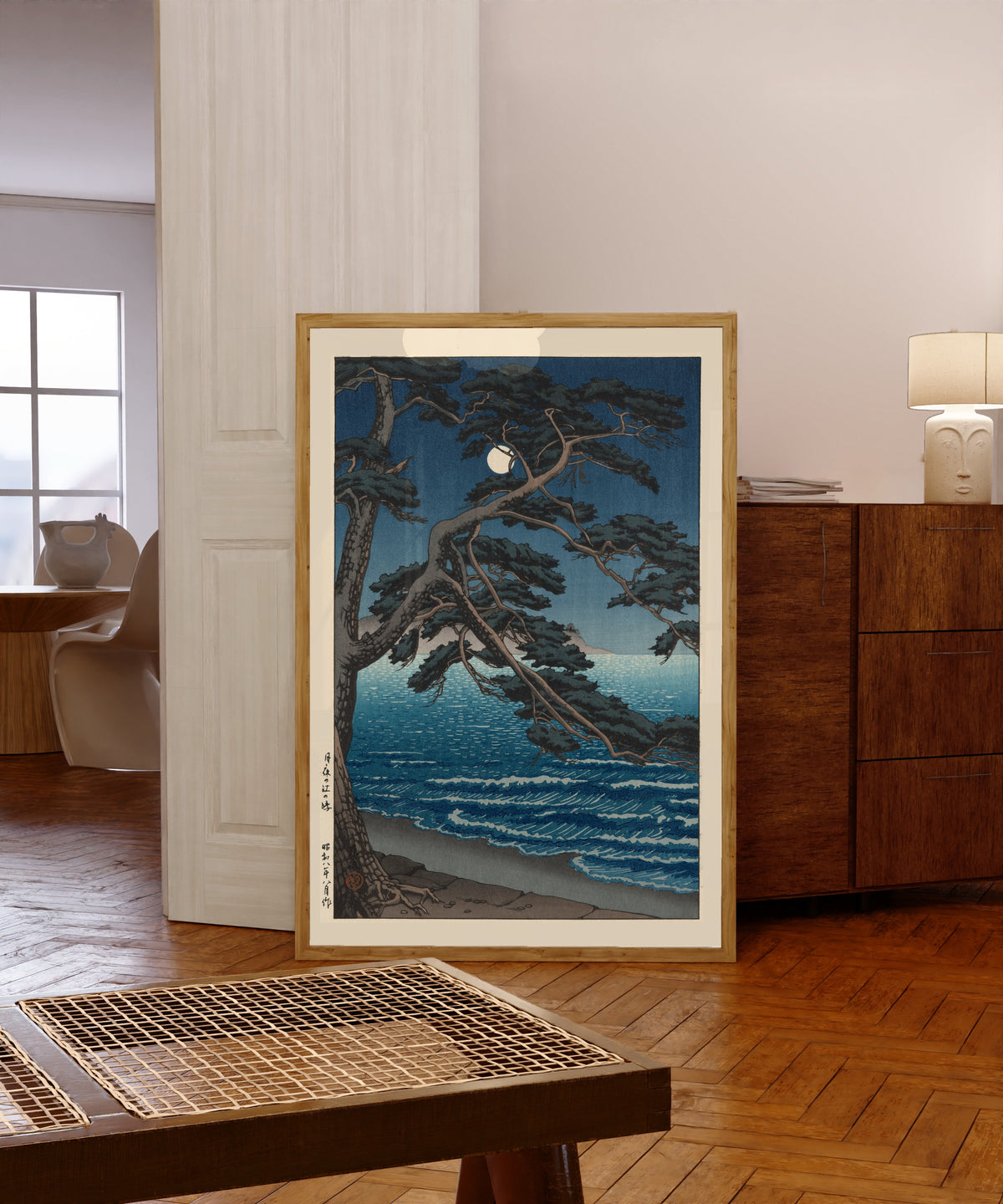 Framed art print of Moon at Enoshima Beach by Kawase Hasui, in a light wood frame leaning in a warm room with a parquet floor