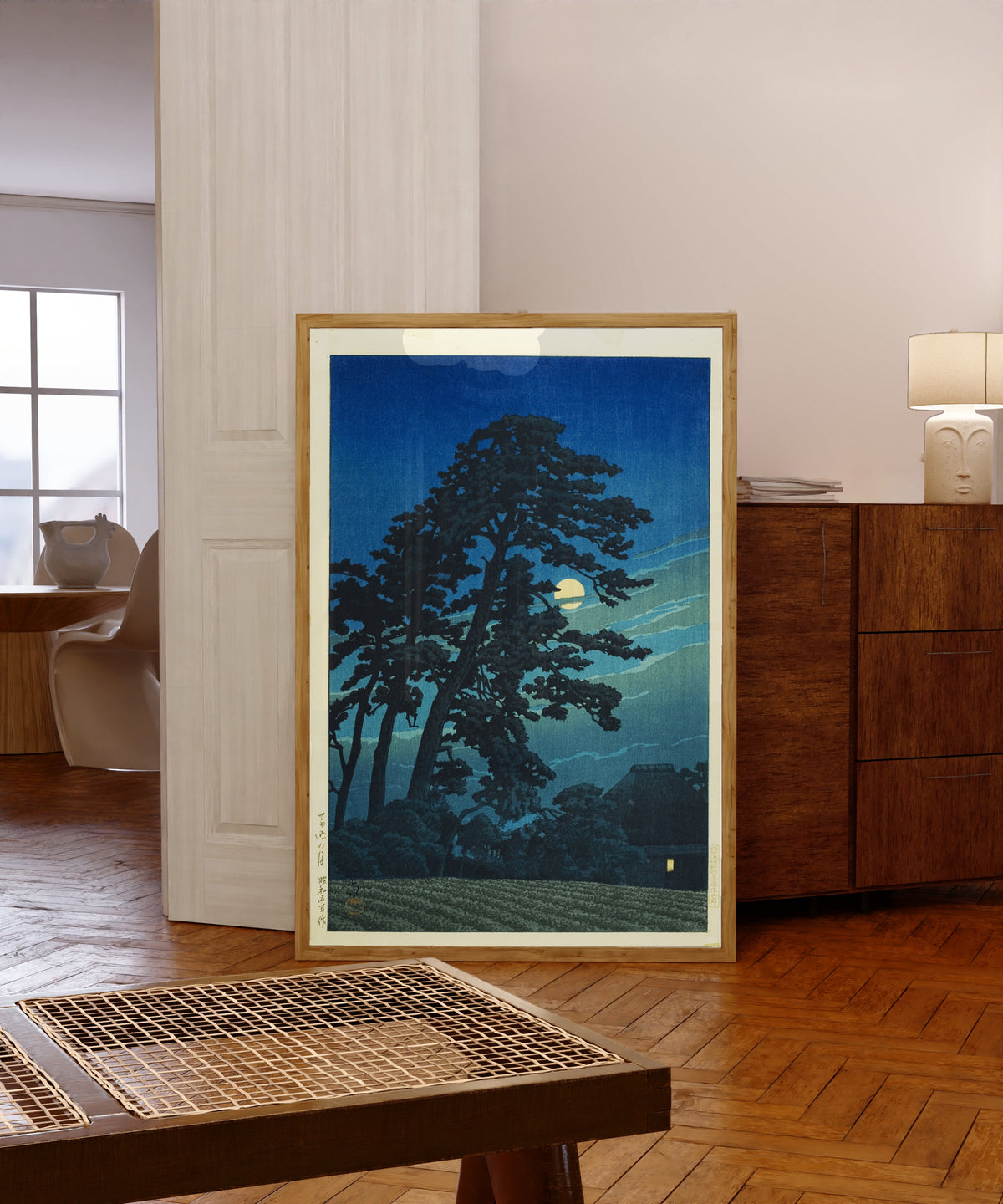 Framed art print of Moon at Umagome by Kawase Hasui, in a light wood frame leaning in a warm room with a parquet floor