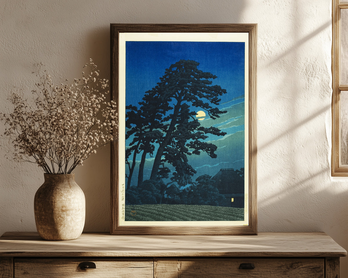 Framed art print of Moon at Umagome by Kawase Hasui, in a dark wood frame leaning on a rustic console beside dried flowers