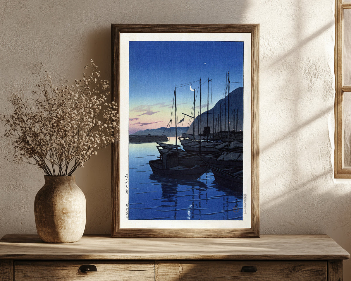Framed art print of Morning in Beppu by Kawase Hasui, in a dark wood frame leaning on a rustic console beside dried flowers