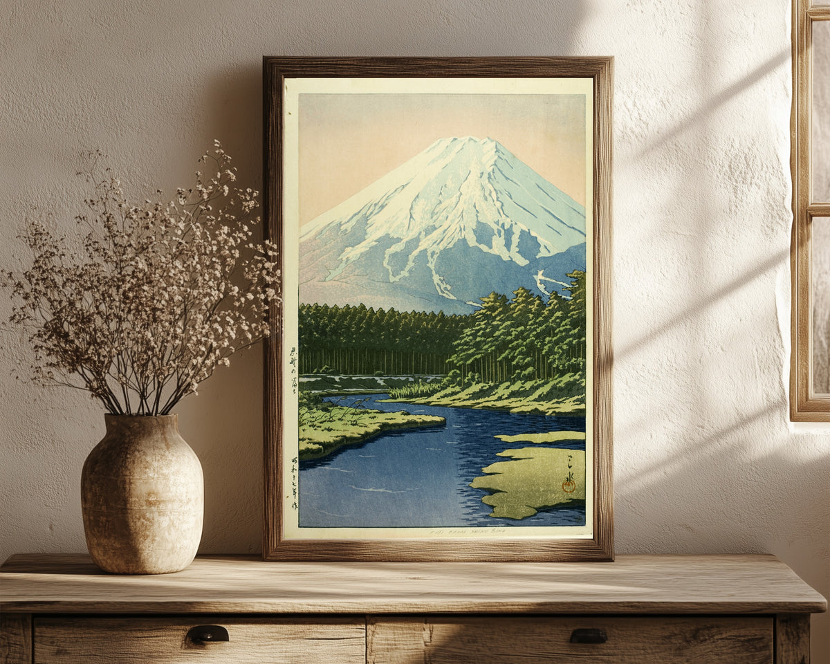 Framed art print of Mount Fuji from Oshino by Kawase Hasui, in a dark wood frame leaning on a rustic console beside dried flowers