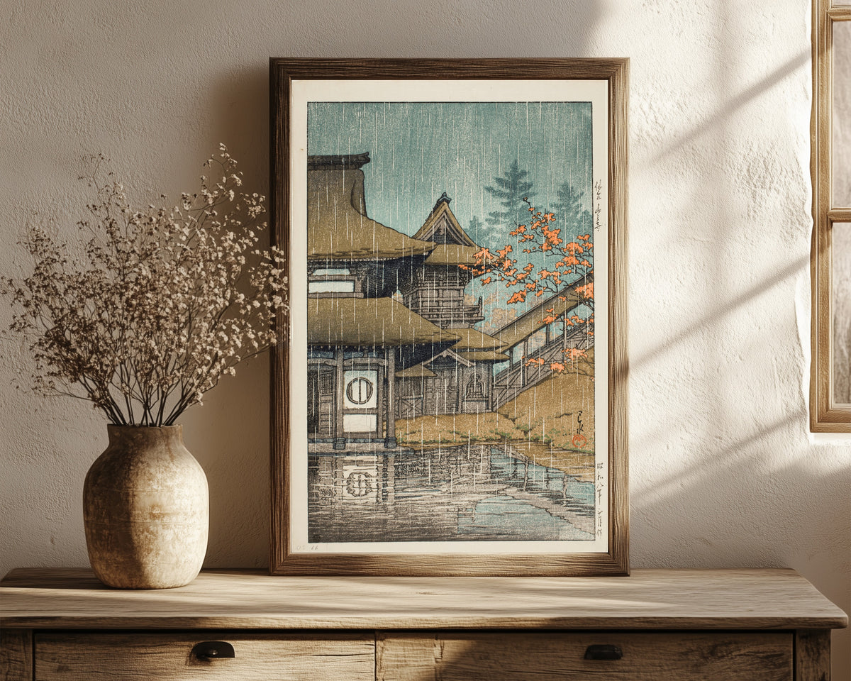 Framed art print of Yamadera Temple in Rain by Kawase Hasui, in a dark wood frame leaning on a rustic console beside dried flowers