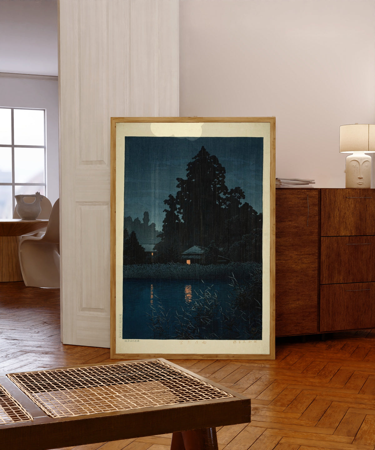 Framed art print of Omiya in the Rain by Kawase Hasui, in a light wood frame leaning in a warm room with a parquet floor