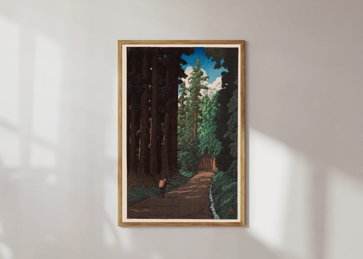 Framed art print of Road to Nikko by Kawase Hasui, in a light wood frame on a sunlit white wall