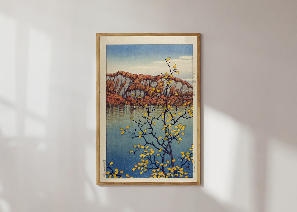 Framed art print of Lake Towada by Kawase Hasui, in a light wood frame on a sunlit white wall