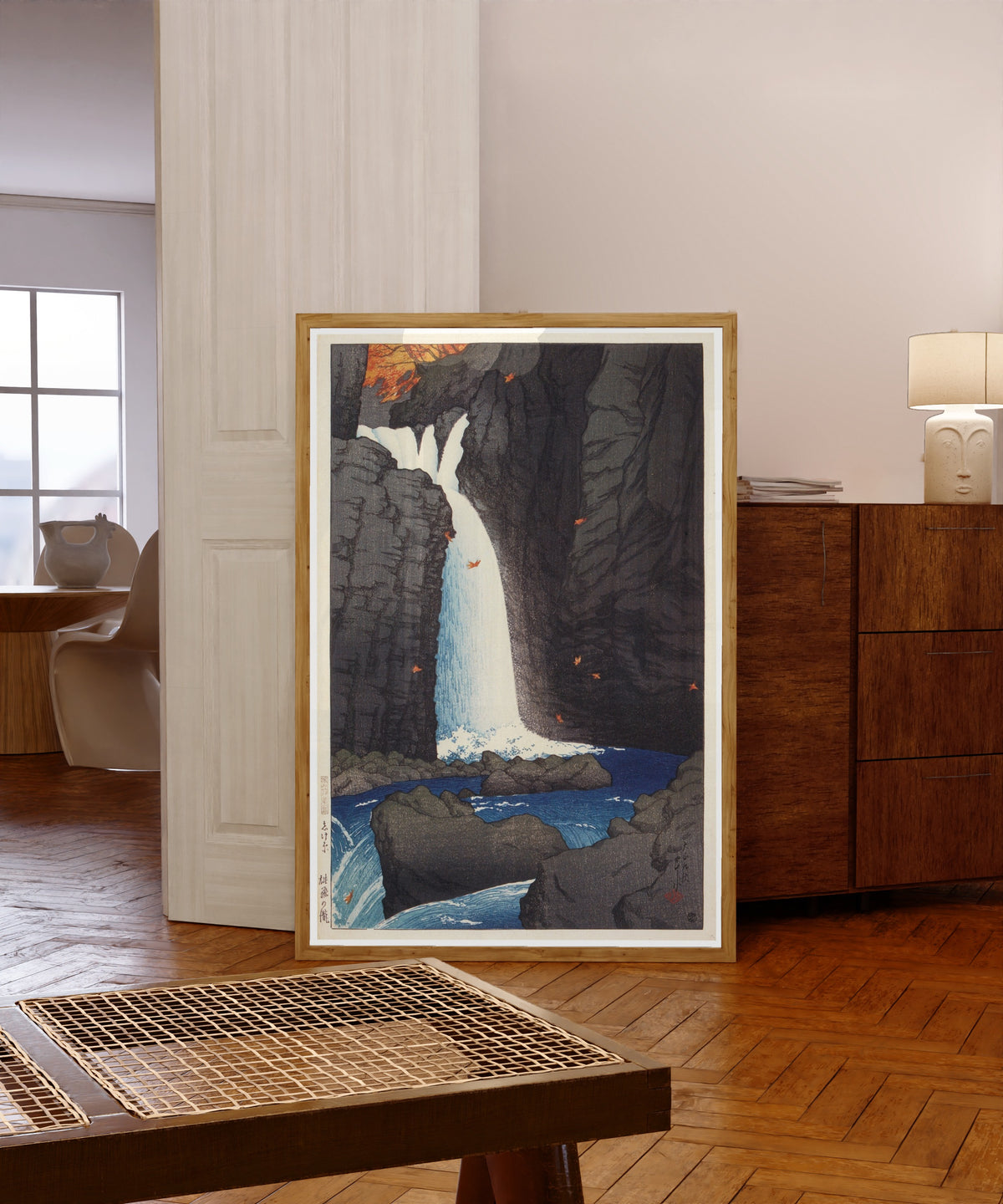 Framed art print of Shihohara Falls by Kawase Hasui, in a light wood frame leaning in a warm room with a parquet floor