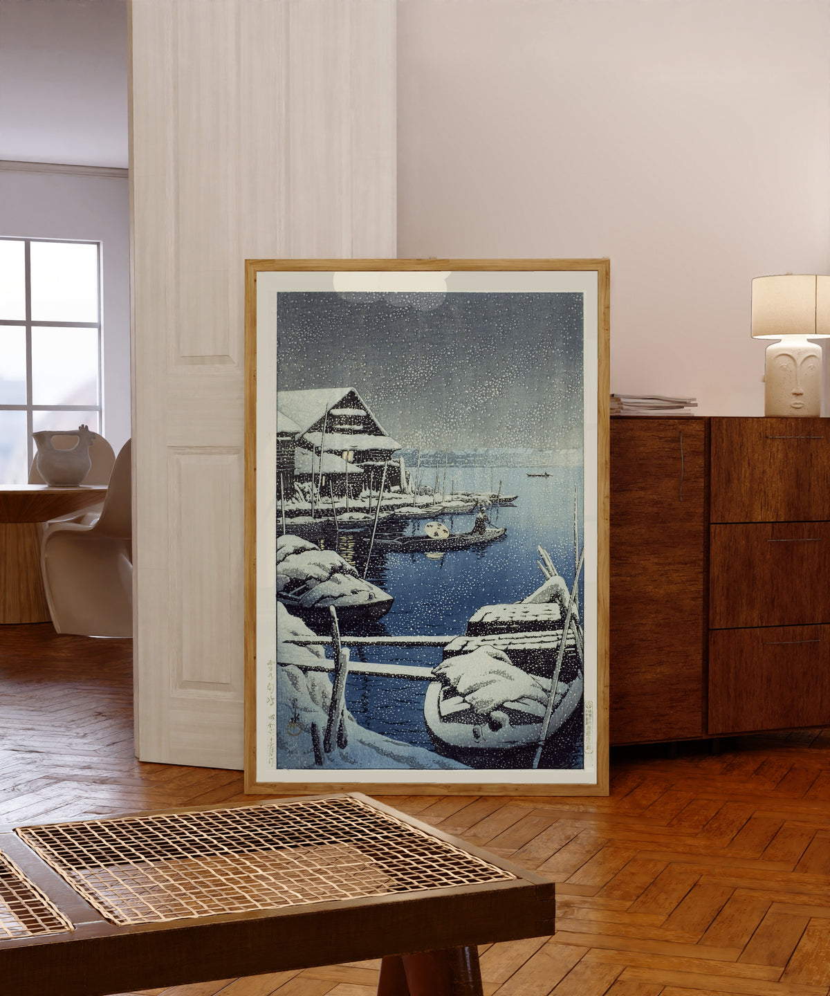 Framed art print of Snow at Mukojima by Kawase Hasui, in a light wood frame leaning in a warm room with a parquet floor