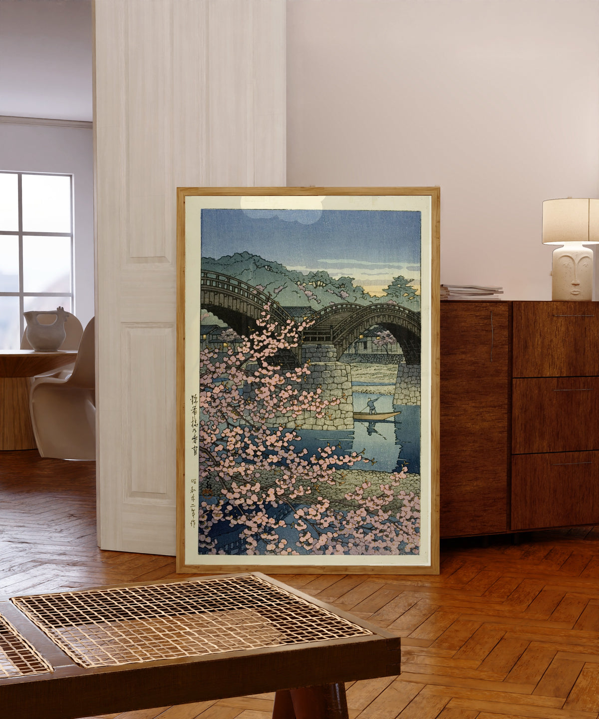 Framed art print of Kintai Bridge Cherry Blossoms by Kawase Hasui, in a light wood frame leaning in a warm room with a parquet floor