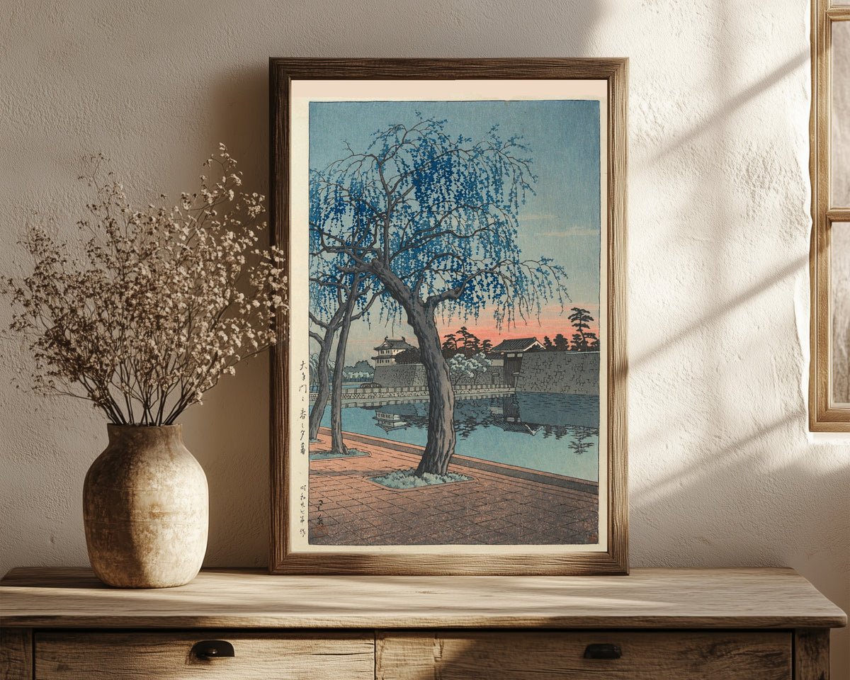 Framed art print of Spring Evening at Otemon Gate by Kawase Hasui, in a dark wood frame leaning on a rustic console beside dried flowers