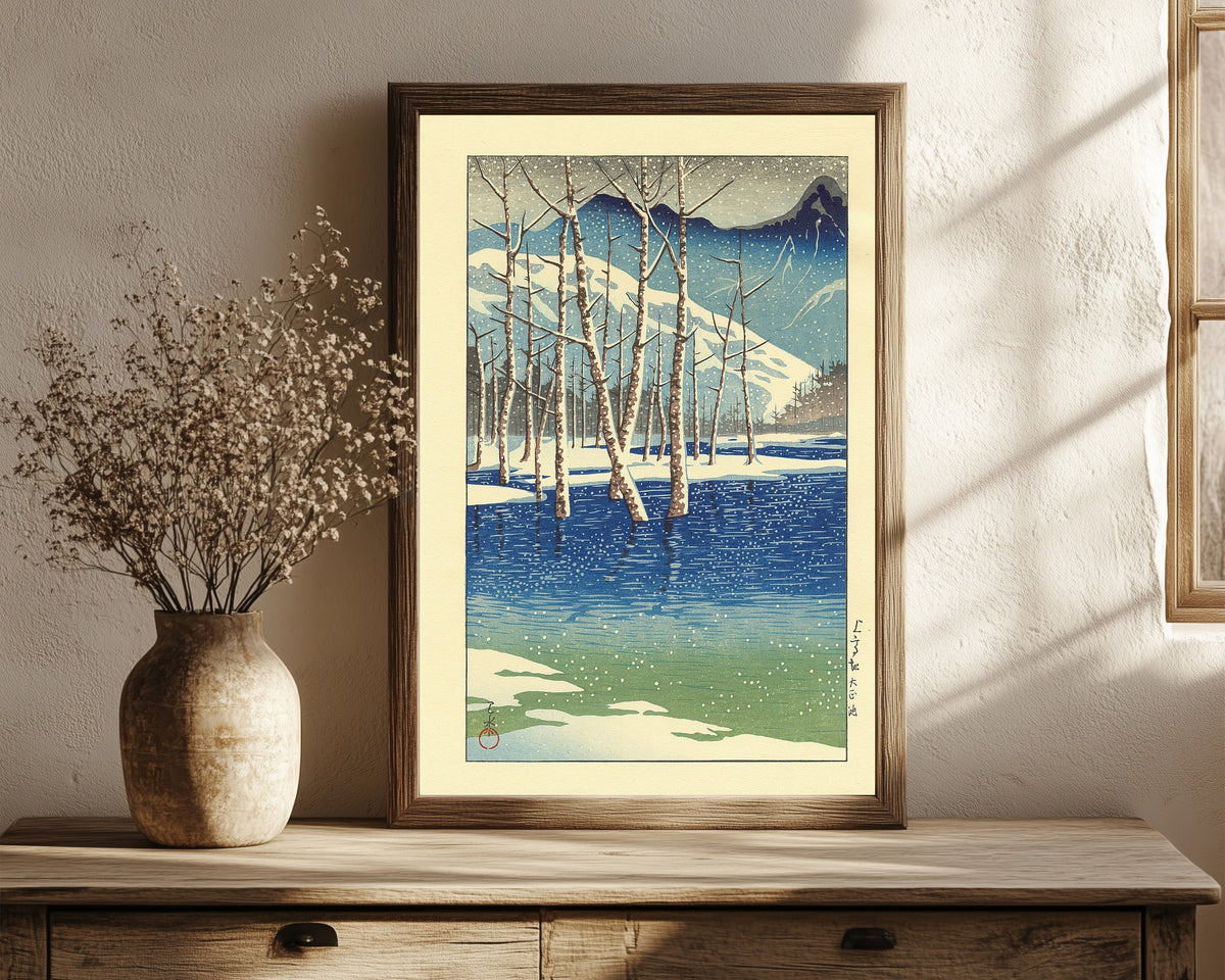 Framed art print of Taisho Pond by Kawase Hasui, in a dark wood frame leaning on a rustic console beside dried flowers