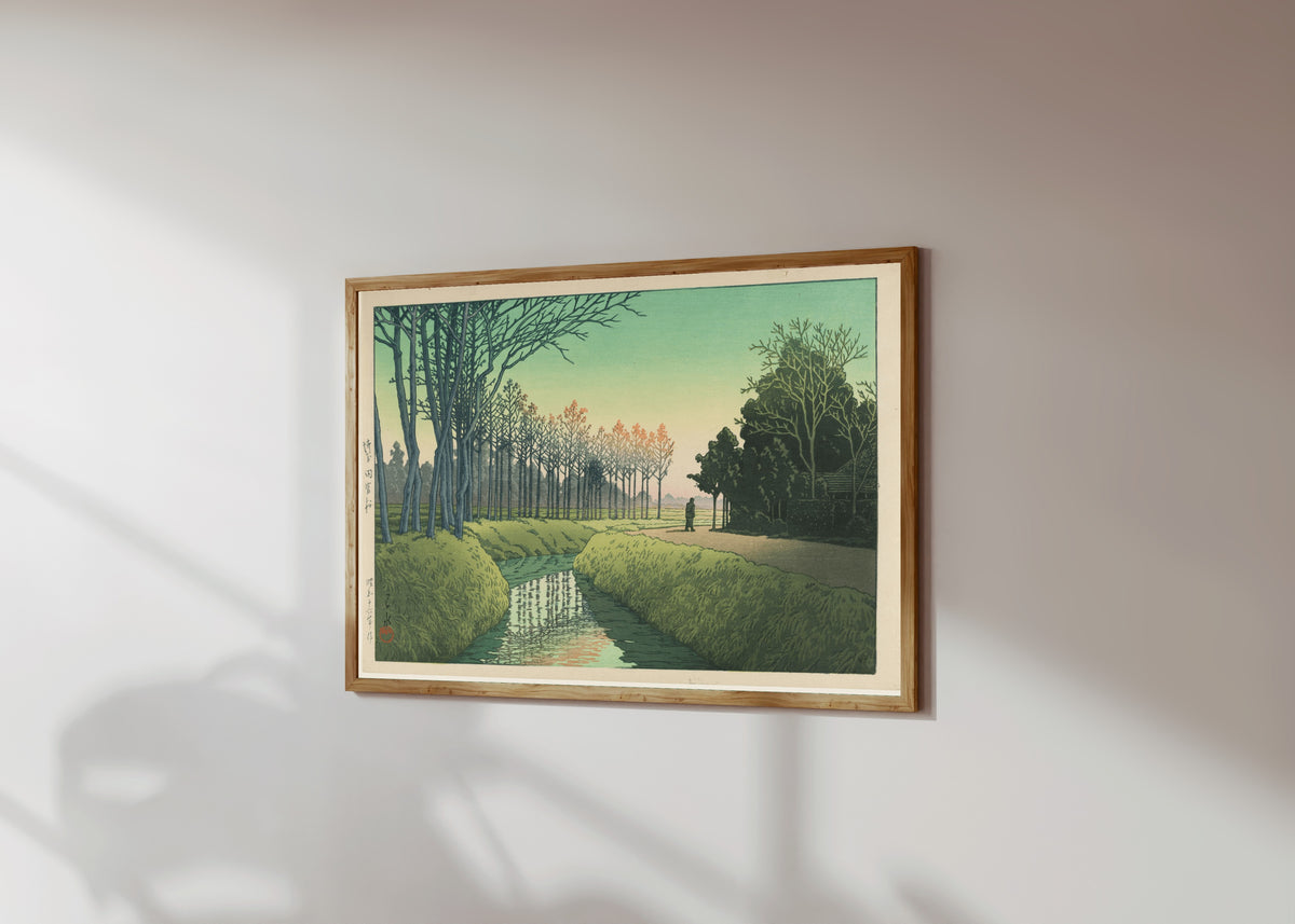 Framed art print of Tamiya Village by Kawase Hasui, in a light wood frame on a sunlit white wall, seen at a slight angle