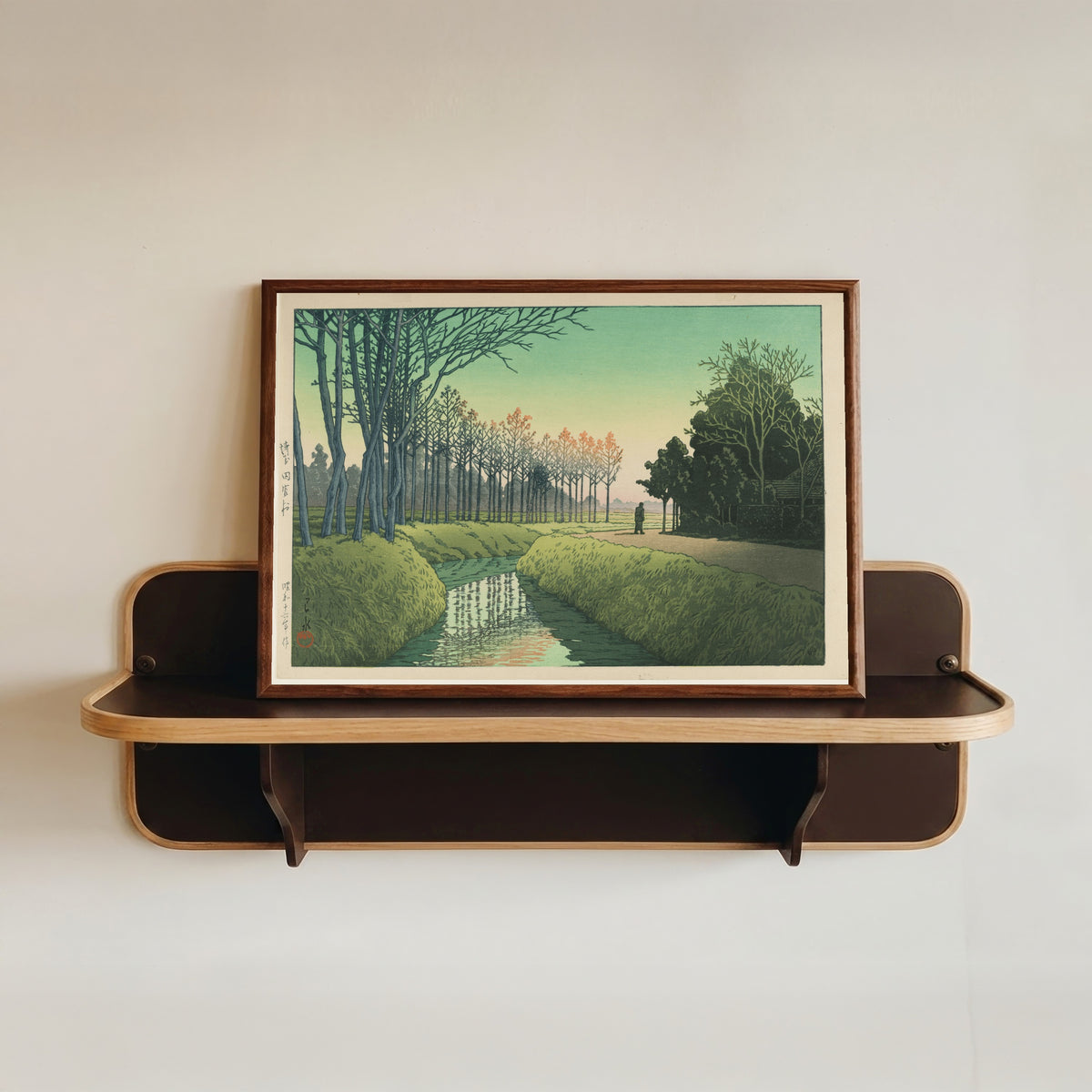 Framed art print of Tamiya Village by Kawase Hasui, in a dark wood frame resting on a wall shelf