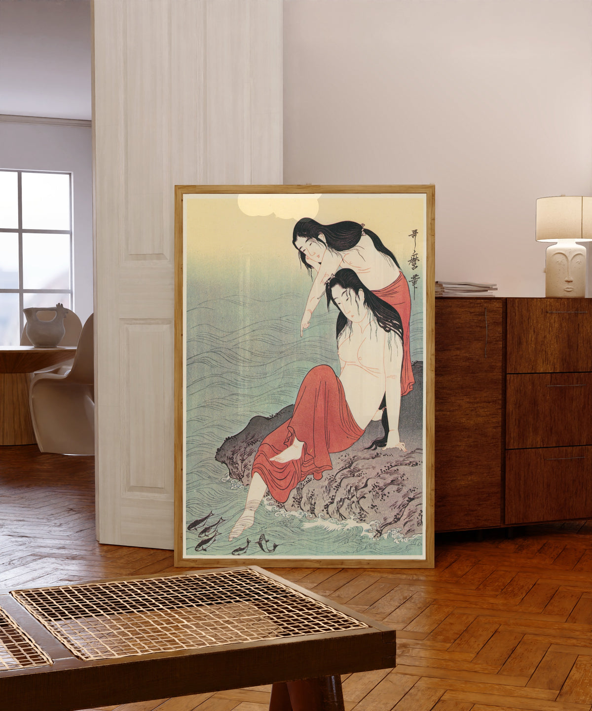 Framed art print of Diving for Abalones (Left) by Kitagawa Utamaro, in a light wood frame leaning in a warm room with a parquet floor