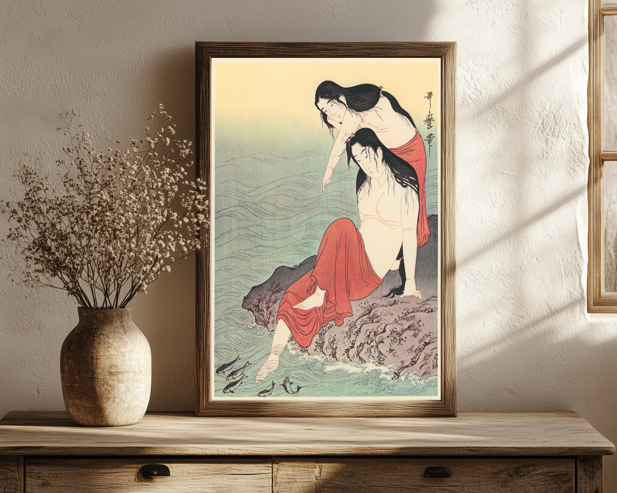 Framed art print of Diving for Abalones (Left) by Kitagawa Utamaro, in a dark wood frame leaning on a rustic console beside dried flowers