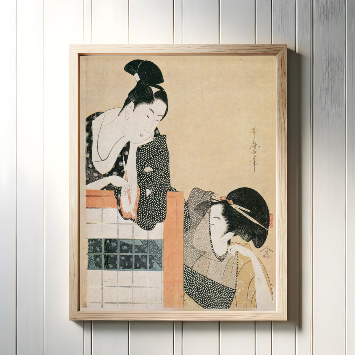 Framed art print of Lovers Behind a Screen by Kitagawa Utamaro, in a light wood frame on a white panelled wall