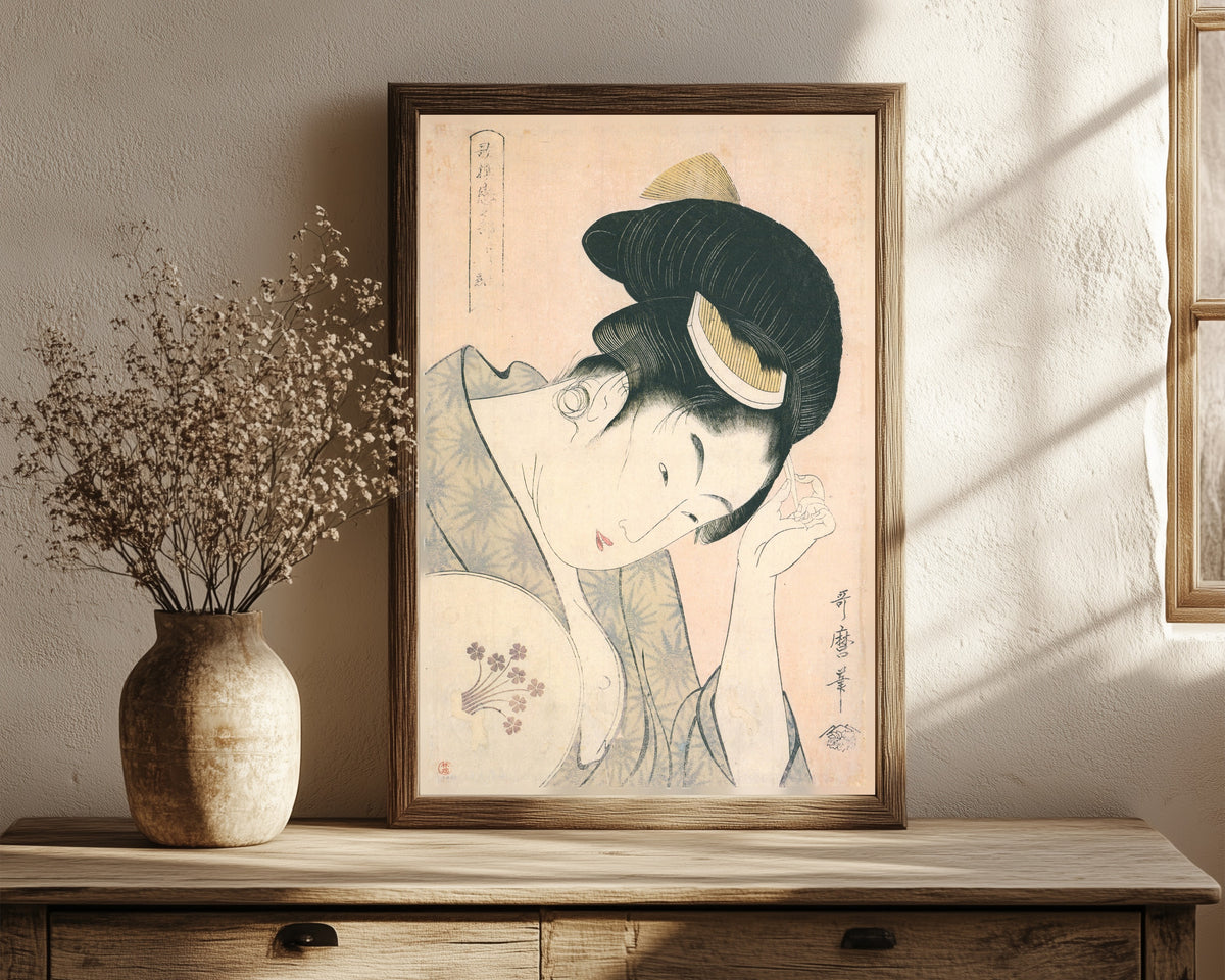 Framed art print of Revealed Love, from Anthology of Poems: The… by Kitagawa Utamaro, in a dark wood frame leaning on a rustic console beside dried flowers