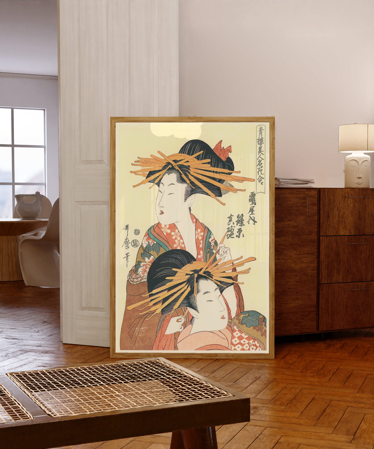 Framed art print of Shinohara and Masagi of the Tsuruya by Kitagawa Utamaro, in a light wood frame leaning in a warm room with a parquet floor