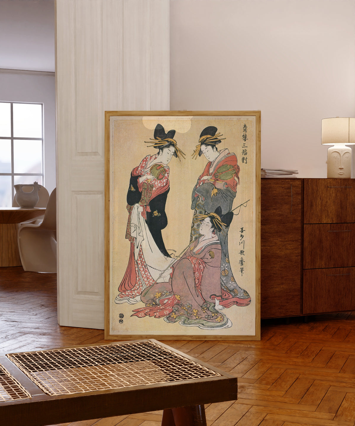 Framed art print of Three Beauties of the Pleasure Quarters (Seiro… by Kitagawa Utamaro, in a light wood frame leaning in a warm room with a parquet floor