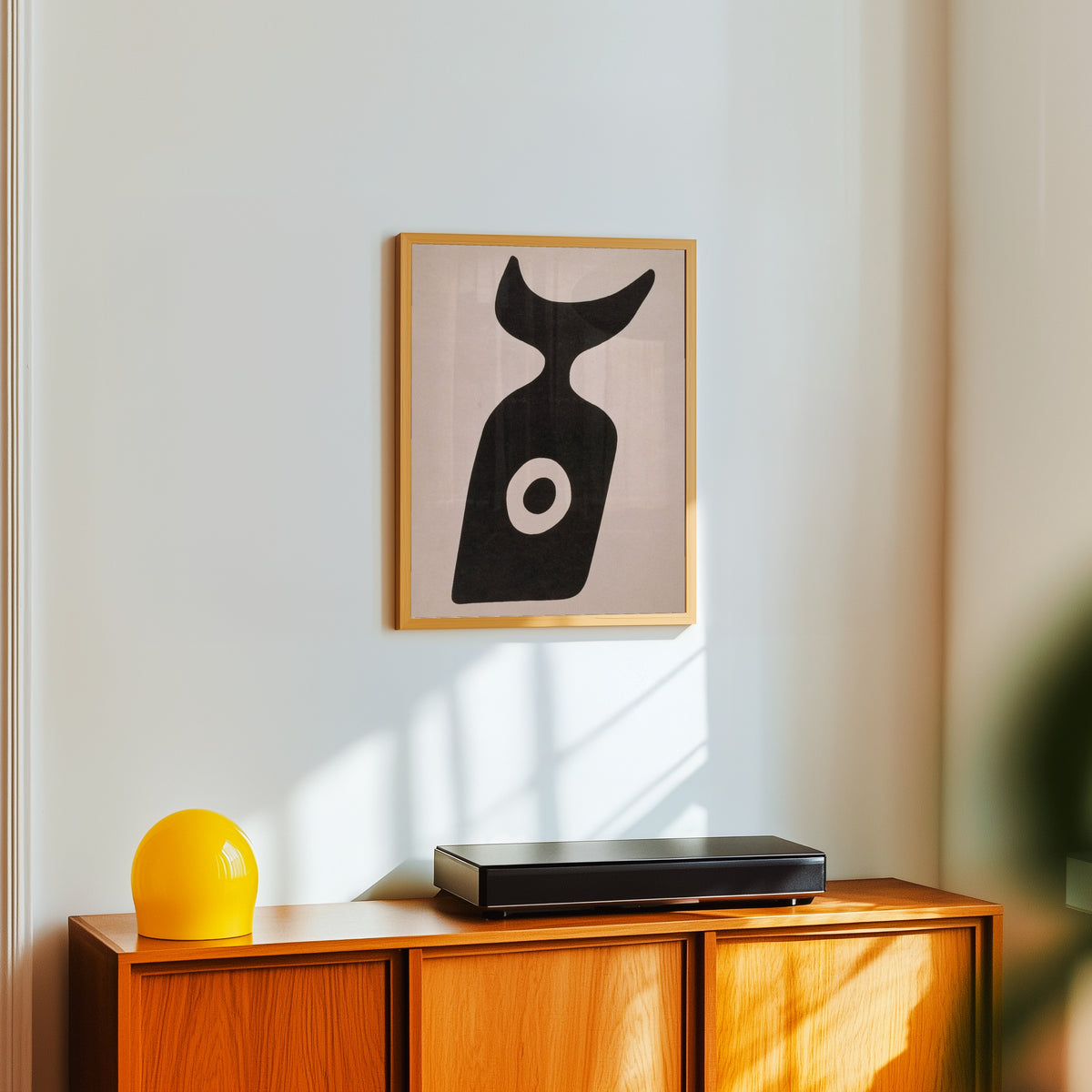 Framed art print of Die Nabelflasche by Kurt Schwitters, in a light wood frame on a white wall above an orange sideboard