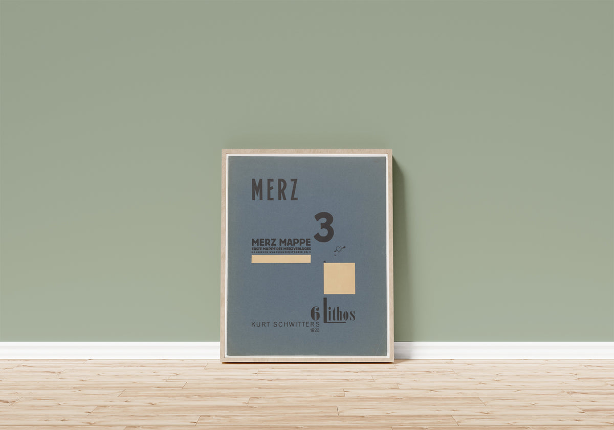 Framed art print of Merz 3. Kurt Schwitters 6 Lithos Pl.1 by Kurt Schwitters, in a light wood frame leaning on a sage green wall above a wooden floor