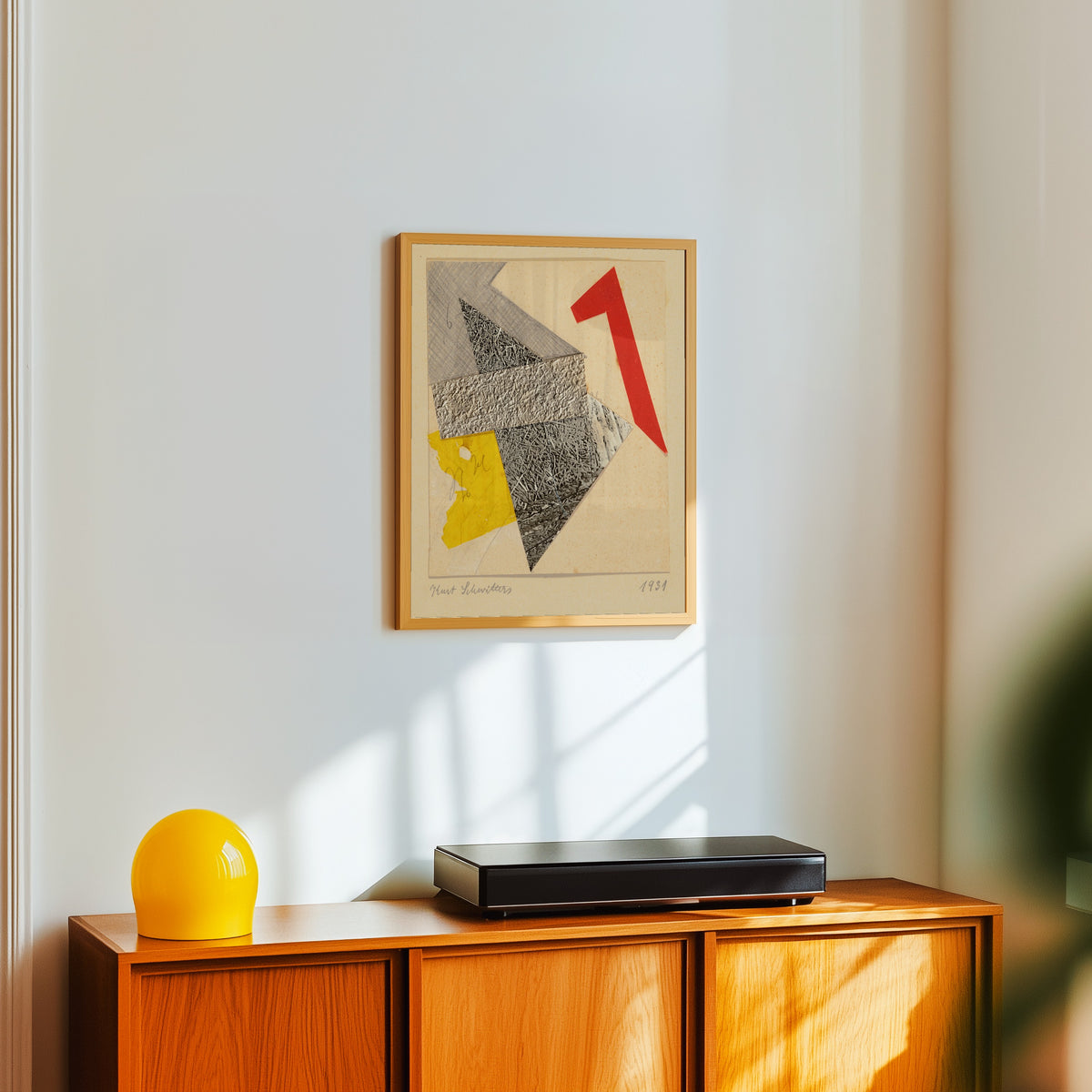 Framed art print of Ohne Titel by Kurt Schwitters, in a light wood frame on a white wall above an orange sideboard