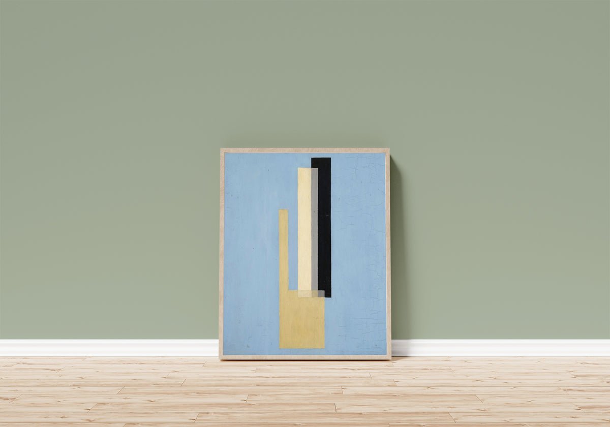 Framed art print of Konstruktion by László Moholy-Nagy, in a light wood frame leaning on a sage green wall above a wooden floor