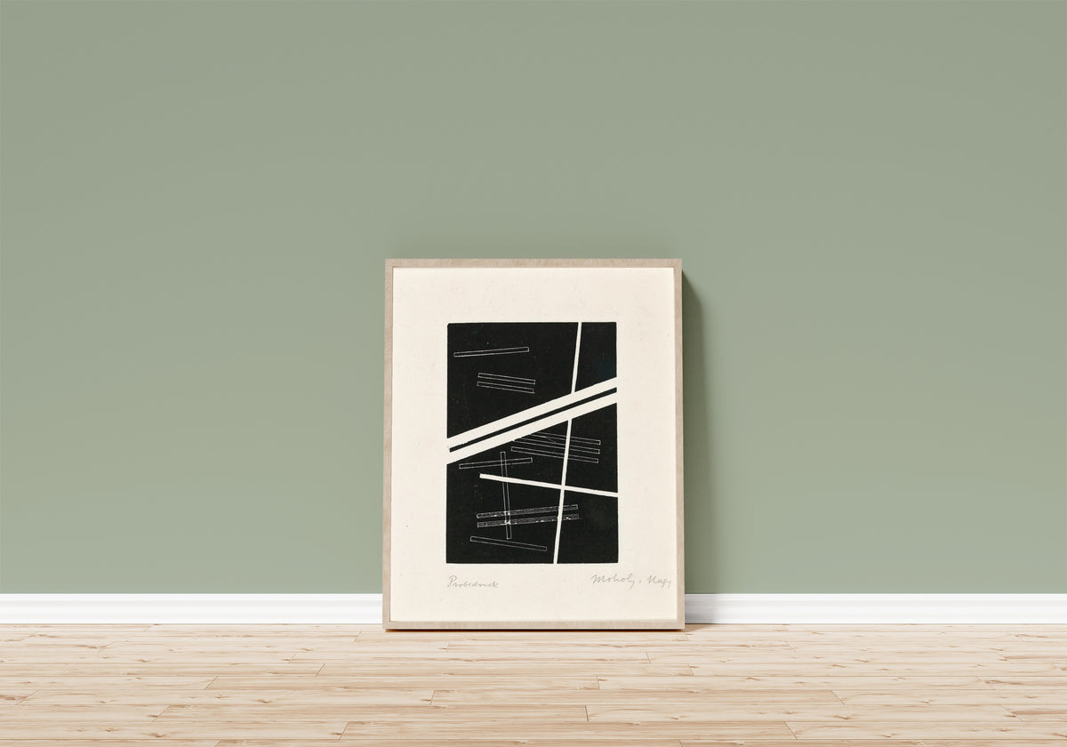 Framed art print of Untitled composition by László Moholy-Nagy, in a light wood frame leaning on a sage green wall above a wooden floor