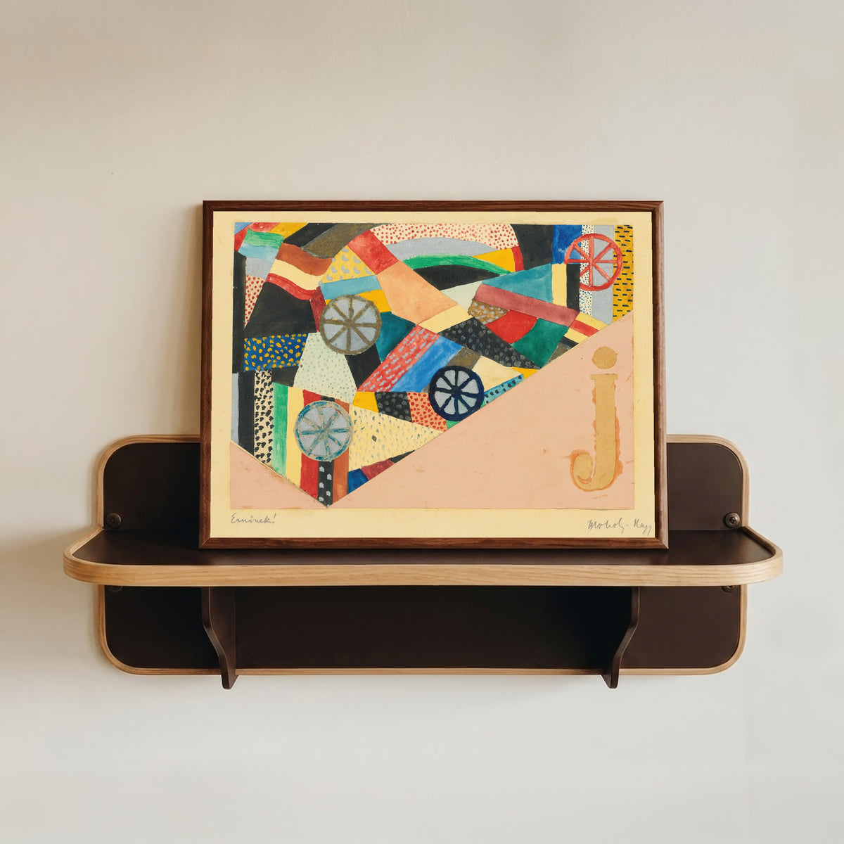 Framed art print of Untitled (J Under Fields, For Ernst Kállai) by László Moholy-Nagy, in a dark wood frame resting on a wall shelf
