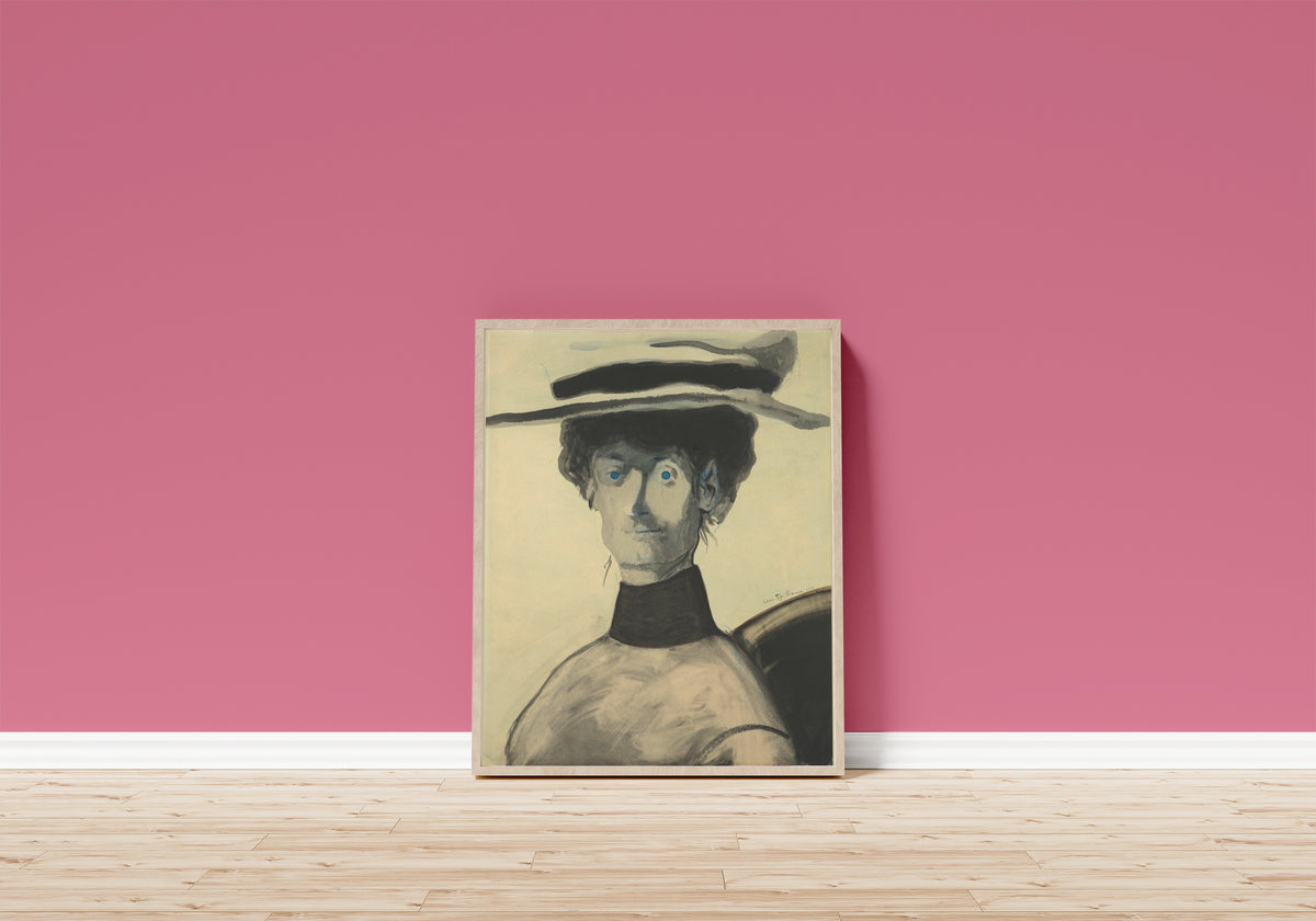 Framed art print of Vrouw met roze hoed by Léon Spilliaert, in a light wood frame leaning on a pink wall above a wooden floor