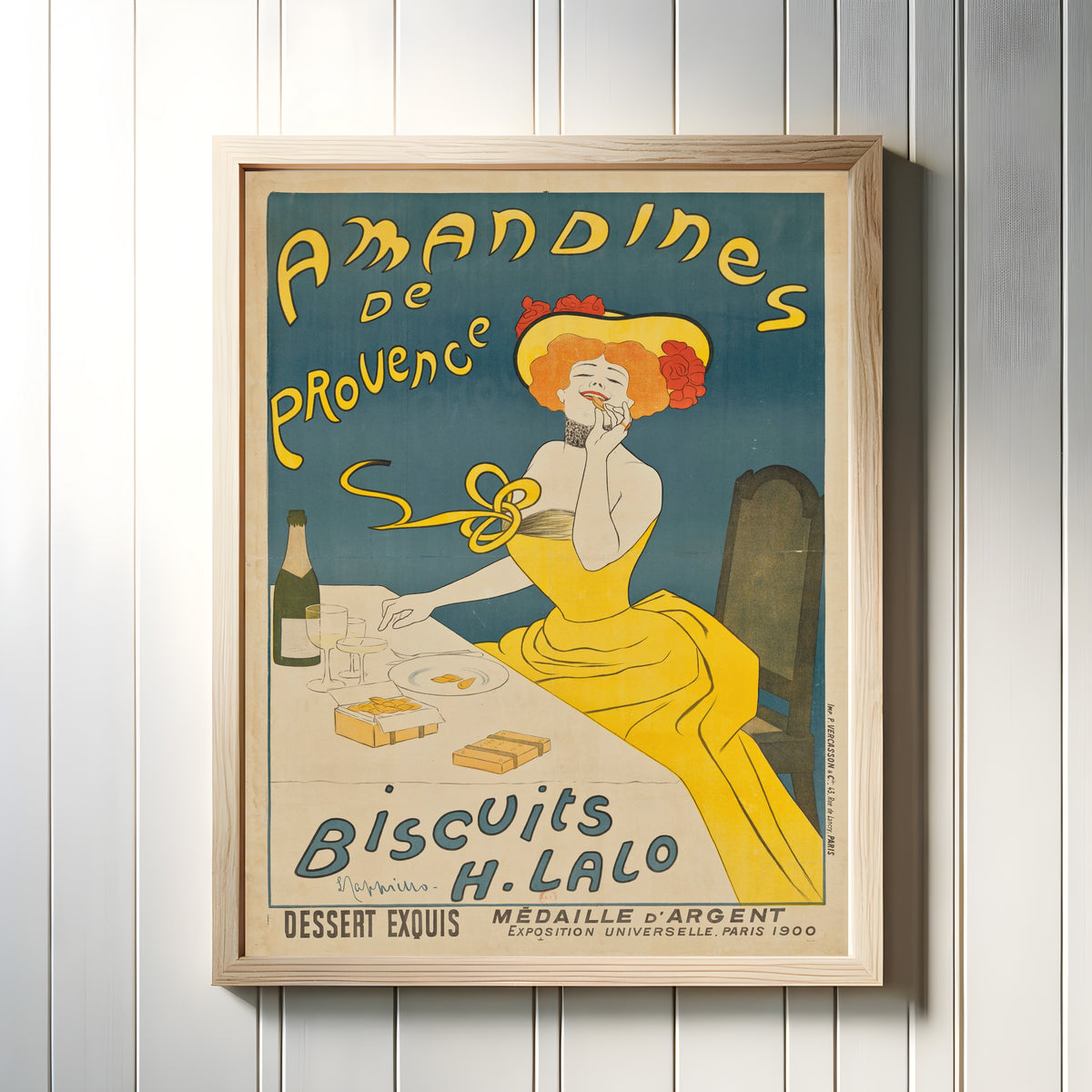 Framed art print of Amandines de Provence by Leonetto Cappiello, in a light wood frame on a white panelled wall