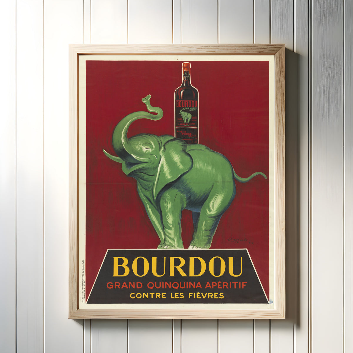 Framed art print of Bourdou grand quinquina apéritif contre les fièvres by Leonetto Cappiello, in a light wood frame on a white panelled wall