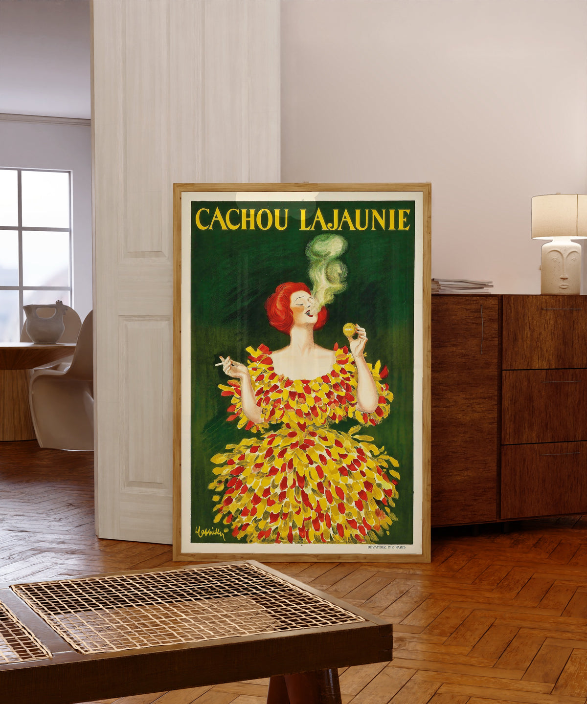 Framed art print of Cachou Lajaunie by Leonetto Cappiello, in a light wood frame leaning in a warm room with a parquet floor