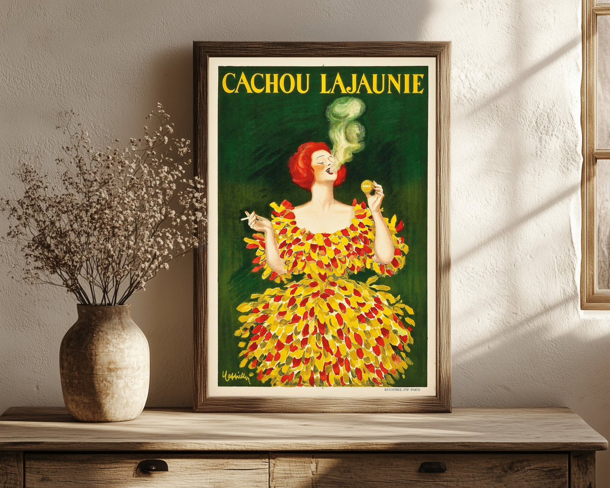 Framed art print of Cachou Lajaunie by Leonetto Cappiello, in a dark wood frame leaning on a rustic console beside dried flowers