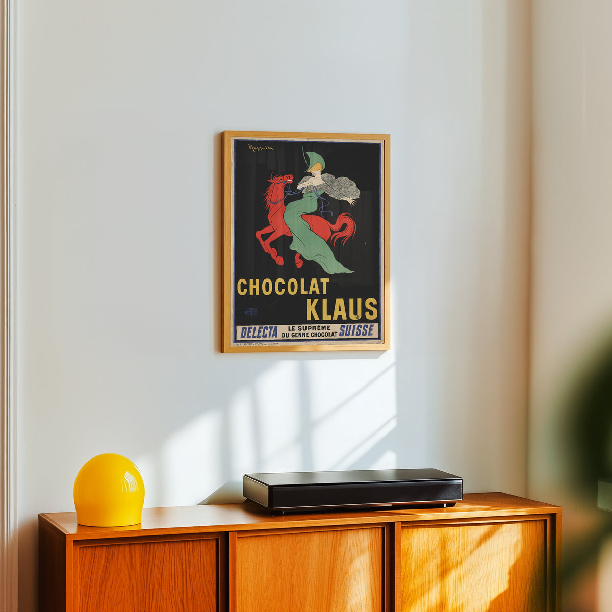 Framed art print of Chocolat Klaus by Leonetto Cappiello, in a light wood frame on a white wall above an orange sideboard