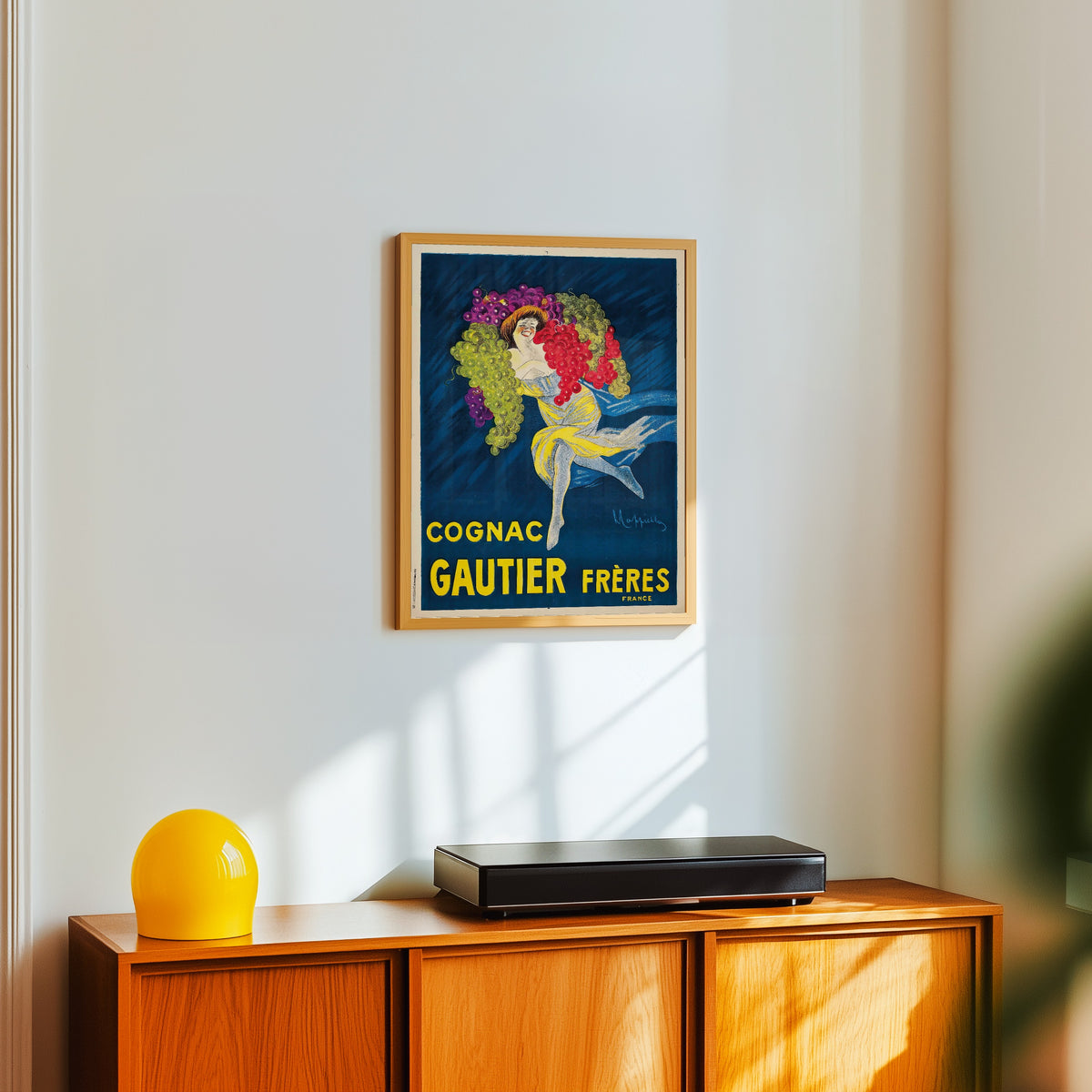 Framed art print of Cognac Gautier Frères by Leonetto Cappiello, in a light wood frame on a white wall above an orange sideboard