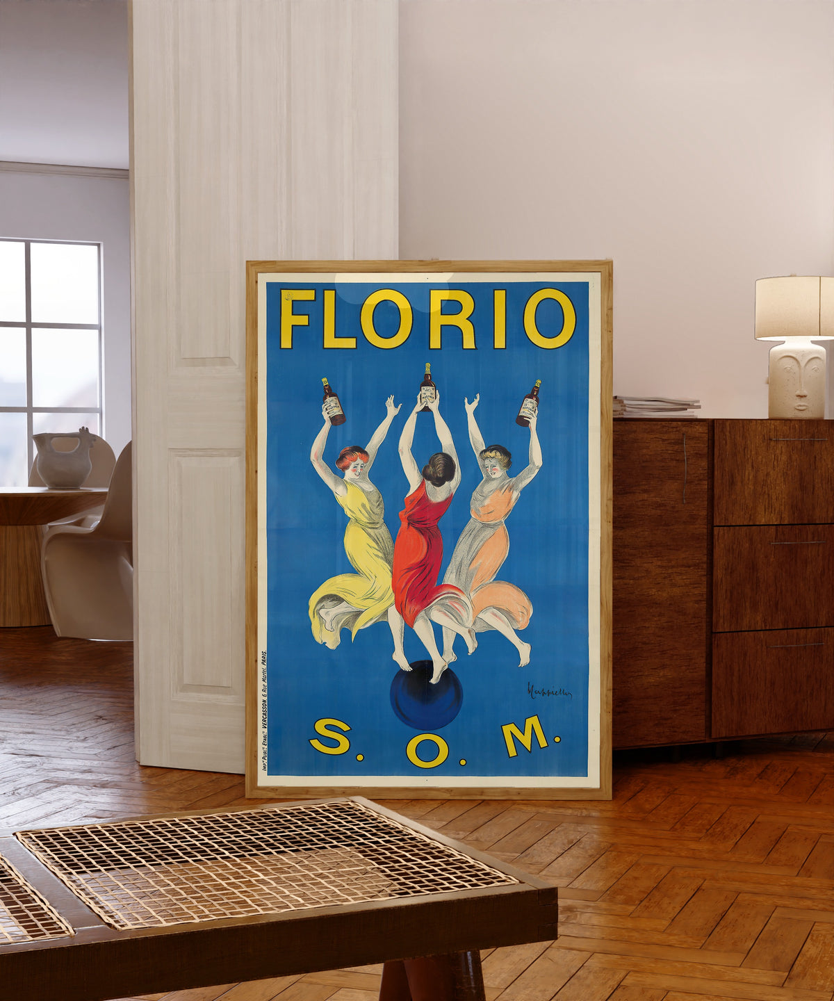 Framed art print of Florio S.O.M. by Leonetto Cappiello, in a light wood frame leaning in a warm room with a parquet floor