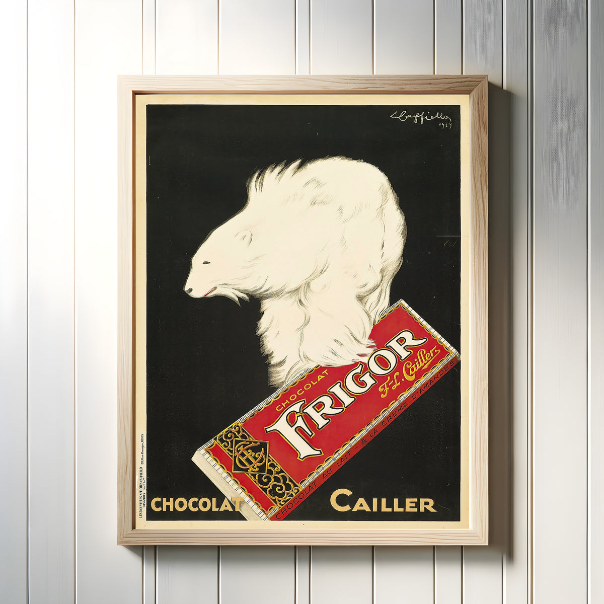 Framed art print of Frigor, Chocolat Cailler by Leonetto Cappiello, in a light wood frame on a white panelled wall