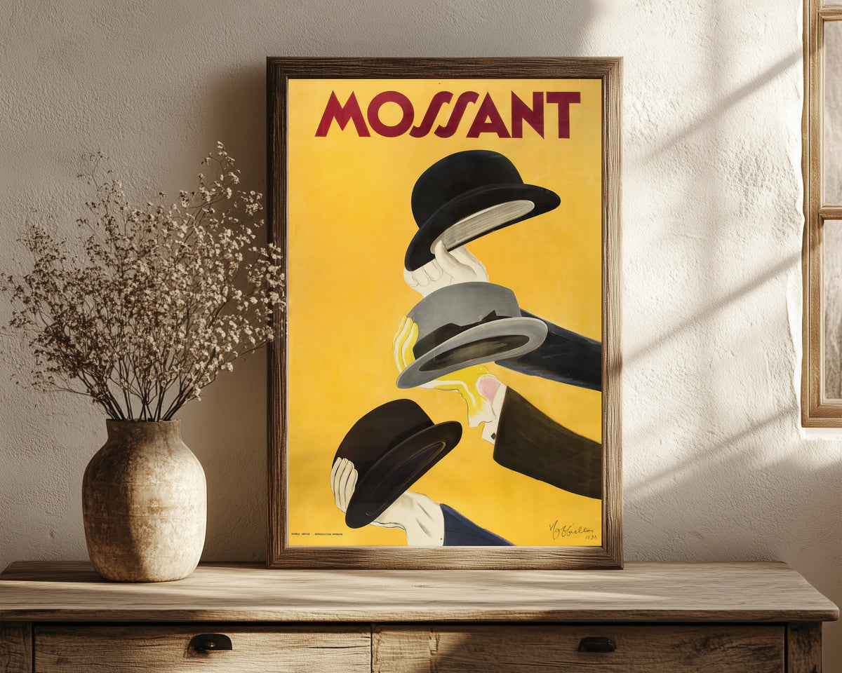 Framed art print of Mossant by Leonetto Cappiello, in a dark wood frame leaning on a rustic console beside dried flowers