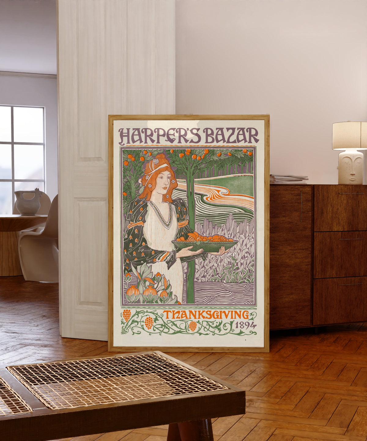 Framed art print of Harper’s Bazar, Thanksgiving 1894 by Louis Rhead, in a light wood frame leaning in a warm room with a parquet floor