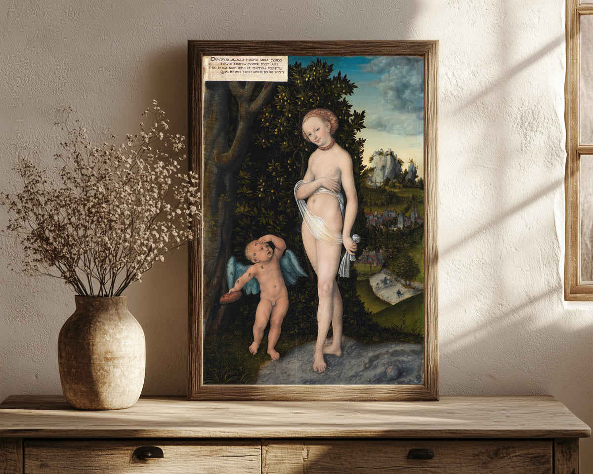 Framed art print of Venus with Cupid Stealing Honey by Lucas Cranach the Elder, in a dark wood frame leaning on a rustic console beside dried flowers