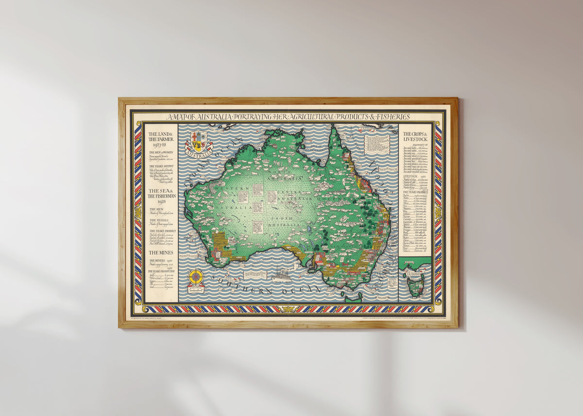 Framed art print of A Map of Australia Portraying Her Agricultural Products & Fisheries by MacDonald Gill, in a light wood frame on a sunlit white wall