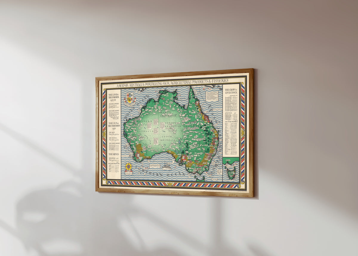 Framed art print of A Map of Australia Portraying Her Agricultural… by MacDonald Gill, in a light wood frame on a sunlit white wall, seen at a slight angle